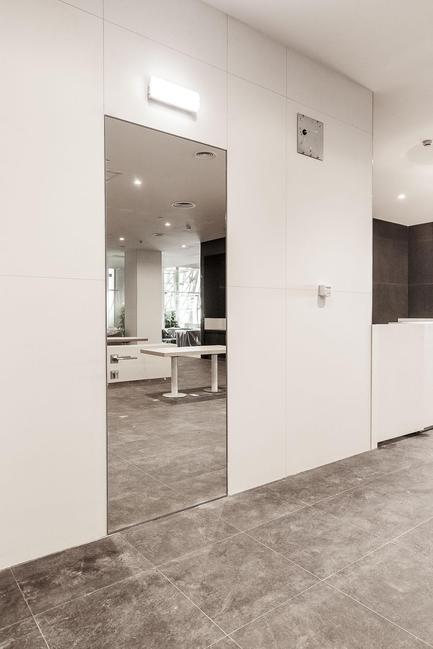 Concealed door with full-height mirror finish blending into modern white wall